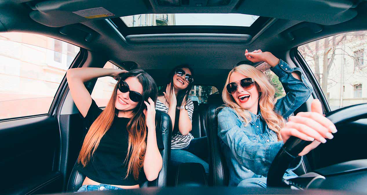 Mujeres jovenes disfrutando de su viaje en carretera sintiéndose seguras por contar con los accesorios básicos en su auto