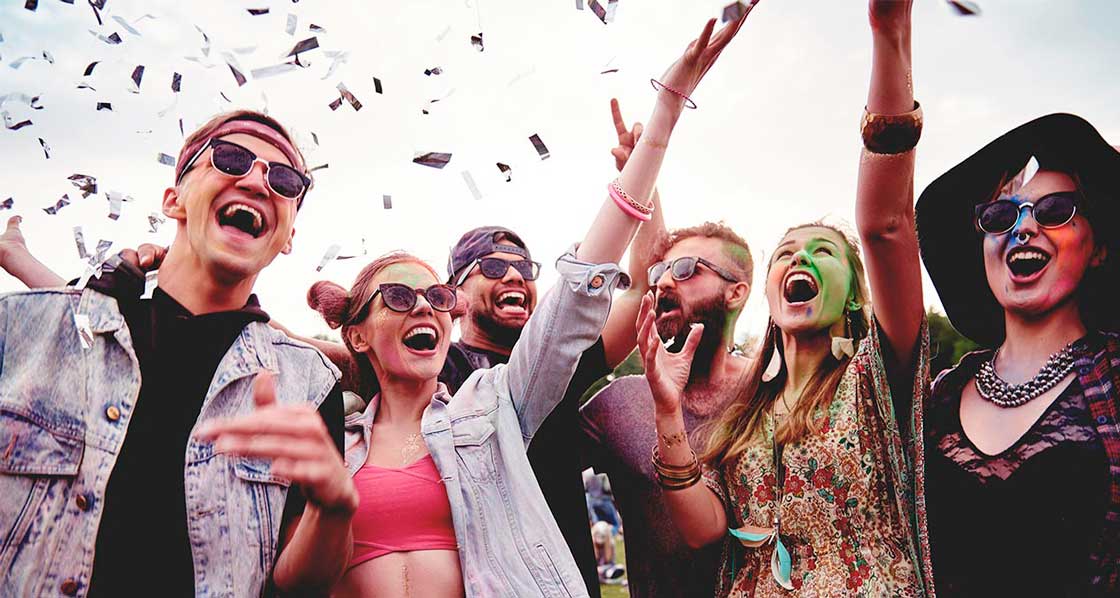 jóvenes sonrientes con color en sus rostros levantan los brazos en un festival de música