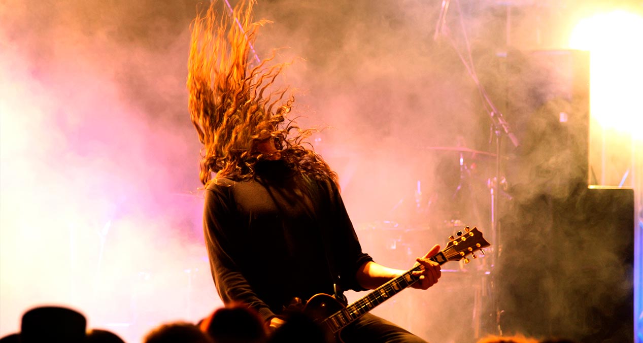 Guitarrista en el escenario agitando su cabello largo en un festival de metal  