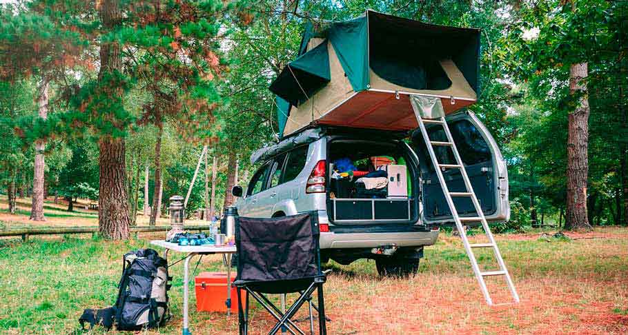 cosas para acampar en un bosque y una tienda de campaña encima de una camioneta gris