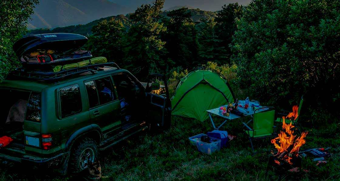 campamento con una tienda de campaña una fogata una mesa y una camioneta verde