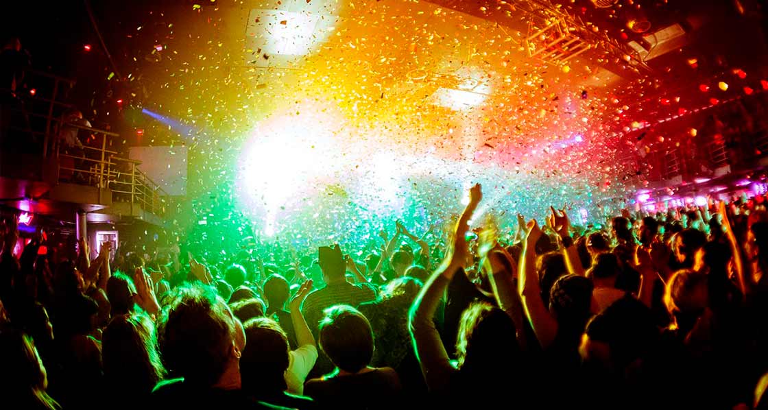 escenario iluminado con luces de color frente a varios espectadores en un festival de música
